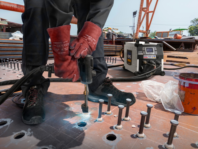 A welder is using a Stud Welding Machine to weld stud bolt on steel plate, at industrial factory.